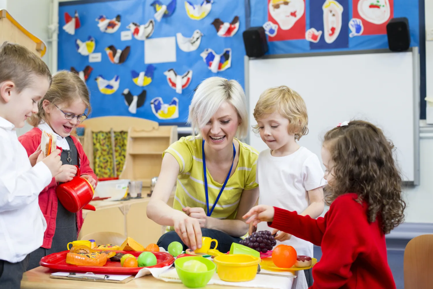 Nursery teacher playing kitchen roleplay with her students in the classroom.