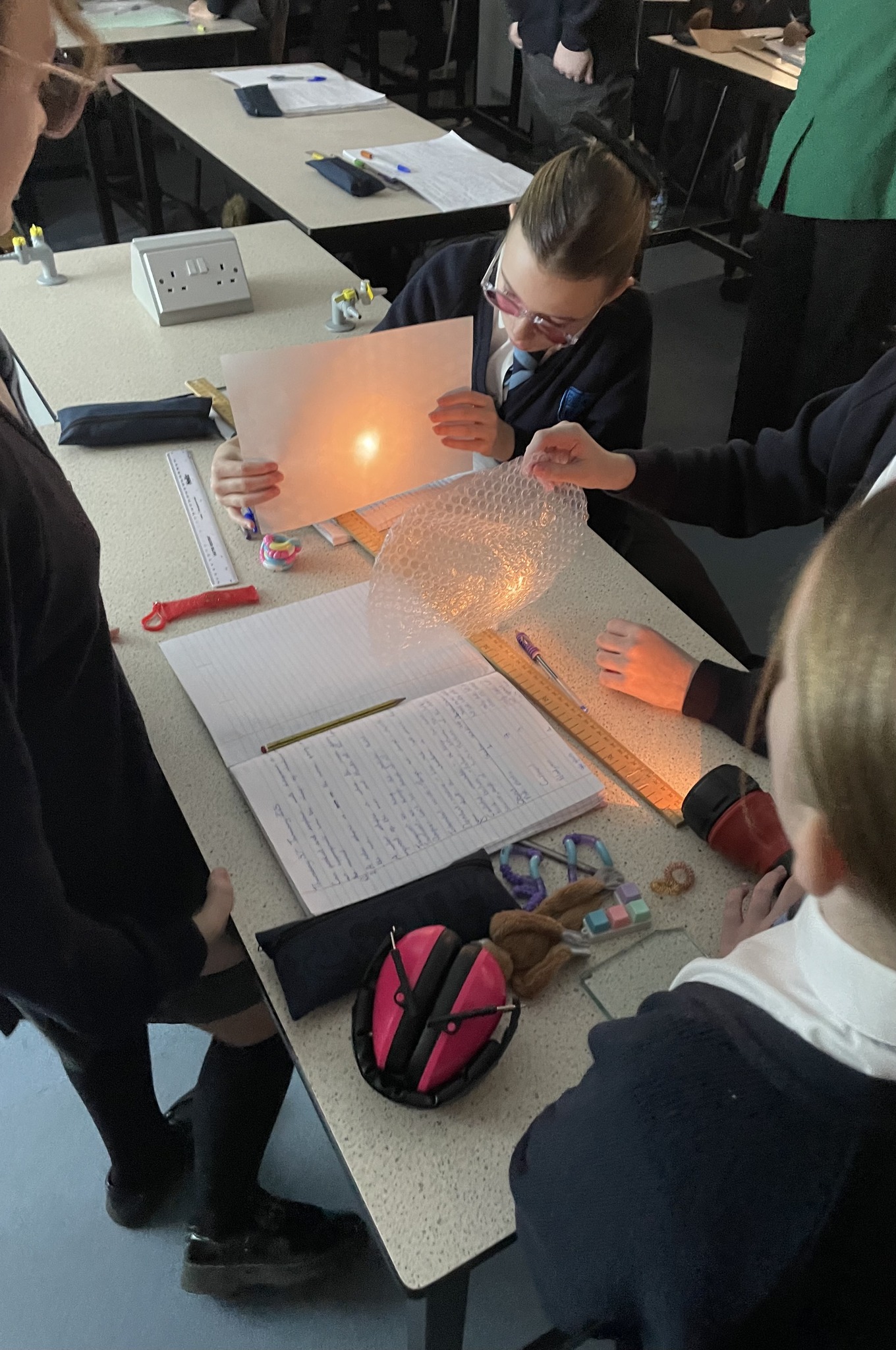 Students at a desk, holding bubble wrap between a piece of paper and a torch